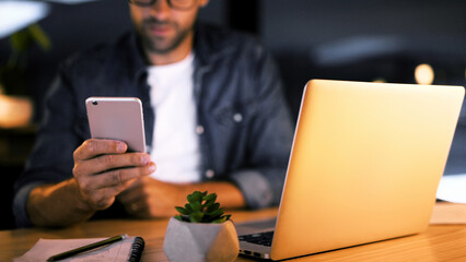 Fototapete - Hands, night and man in office, cellphone and message to contact, social media and communication. Person, closeup and employee in workplace, evening and smartphone with digital app, texting or laptop
