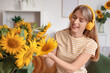 © Pixel-Shot - Beautiful young happy woman in headphones with bouquets of sunflowers at home