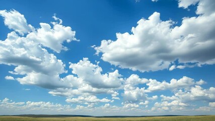 Wall Mural - Fluffy white clouds in a bright blue sky over a vast grassland landscape