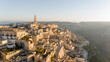 © rh2010 - Aerial view of Matera, Italy, bathed in golden morning light. The iconic stone dwellings and cathedral tower rise above the canyon, showcasing this UNESCO-listed historic wonder