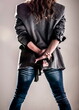 © Marcos - A person, seen from the back, is holding a gun behind their back. They are wearing a blazer and jeans.