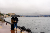 A young couple with umbrellas in their hands look out over the Bosphorus Bridge in rainy weather