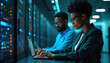 © Pete - Black woman, man using laptop, working server room. African-American professionals collaborate on tech project. Data center specialists, IT infrastructure management, modern computing, online service.