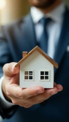 Aufkleber - A man in a business attire holds a scale model of a house, possibly for real estate or architecture purposes