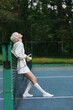 © SHOTPRIME STUDIO - Young female tennis player in stylish sportswear enjoying a moment of relaxation on the court, showcasing a vibrant and seasonal outdoor atmosphere