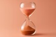 © Rifqi - A close-up shot of an hourglass with peach-colored sand against a muted peach background, concept for time management, deadline, and urgency
