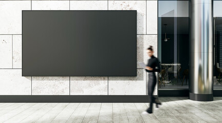 Poster - Blank black billboard on modern stone building exterior with blurred businesswoman walking past in daylight urban setting outdoors concept.
