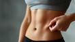 © BB_Stock - Toned female abdomen with hand pinching skin, fitness and healthy body concept, close up of slim waist and belly, natural skin texture visible, wearing gray sports top and black pants