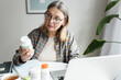 © shurkin_son - Aged woman holding bottle of dietary supplement and reading label with instruction, ingredients or brand name carefully before ordering vitamins online using laptop and web application