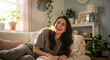 © Evans - Happy young brunette woman laughing genuinely while lounging comfortably on a sofa in a bright, sunlit living room. Relaxed lifestyle, contentment, and joyful moments at home.