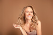 © Beauty Hero - Charming mature blonde woman smiling brightly while posing gracefully against a soft beige background