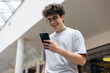 © Светлана Мищенко - Smiling teenage boy using smartphone in modern urban space. Concept of youth lifestyle, digital communication, mobile technology, and social media engagement. texting, browsing social media, chatting