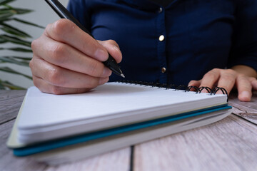 Poster - A person is writing in an open notebook, holding the pen with one hand and sitting at their desk. 