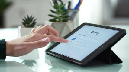 Poster - Close Up Of A Hand Touching Black Tablet Screen On A Light Green Table With Small Potted Plants in Background
