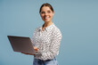 © Maria Vitkovska - Smiling businesswoman holding laptop and looking away on blue background
