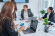 © panomporn - Group of business partners gathered around open laptop discussing company development strategies in modern office.