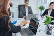 © panomporn - Group of business partners gathered around open laptop discussing company development strategies in modern office.
