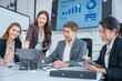 © panomporn - Group of business partners gathered around open laptop discussing company development strategies in modern office.