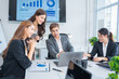 © panomporn - Group of business partners gathered around open laptop discussing company development strategies in modern office.