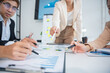 © panomporn - Group of confident professional business people pointing at graphs and charts to analyze marketing data to plan new sales strategies to increase productivity in modern office.