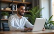 © li - Smiling indian business man working on laptop at home office. Young indian student or remote teacher using computer remote studying, virtual training, watching online education webinar at home office.