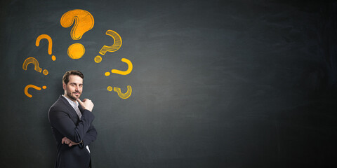 Poster - Confident businessman thinking with hand-drawn yellow question marks on black chalkboard background, representing curiosity and creative problem-solving.