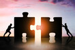 © Who is Danny - Silhouettes of businesspeople pushing giant puzzle pieces together at sunset to represent teamwork and collaboration in a business concept.