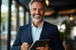 © btiger - smiling mature businessman in glasses wearing dark blazer using digital tablet in modern office environment with natural light