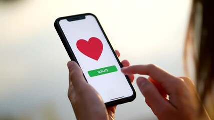 Poster - Person Taps Start Button on Smartphone with Red Heart on White Display in Soft Outdoor Light
