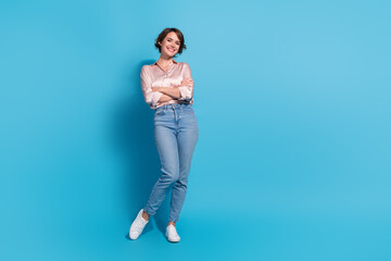 Poster - Charming young woman in stylish pink blouse standing confidently with a delightful smile against a vibrant blue background