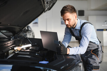 Fototapete - Friendly mechanic in modern car repair shop with car. Professional technician checking vehicle diagnostics and maintenance. Concept of automotive industry and customer service