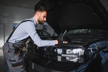 Fototapete - Mechanic Uses a Computer with an Augmented Reality Diagnostics Software. Specialist Inspecting Car's Engine to Quickly Spot Broken Components. Premium Car Service