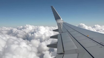 Poster - Aircraft wing soaring above pristine white cloud layer during bright sunny day, revealing extended ailerons and wing flaps against expansive blue sky backdrop