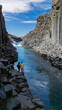 © Fokke Baarssen - Adventurers stand by the crystal-clear waters of Studlagil Canyon, surrounded by towering basalt columns and rugged cliffs in Iceland.