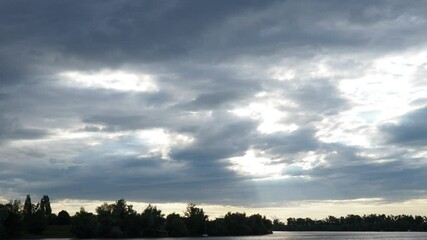 Poster - Witness natures beauty as vibrant beams of light ripple across the tranquil river landscape, creating an enchanting interplay of sunlight and clouds over time