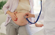 © Studio Romantic - Gynecologist examining heartbeat in the abdomen of pregnant young woman sitting on couch in medical clinic. Obstetrician doctor or nurse checking her patient expecting a baby. Pregnancy concept.