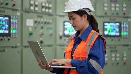 Poster - Asian Female Engineer Uses Laptop in Front of Control Panel Wearing Blue Uniform and Safety Gear at Industrial Site