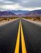 © Tori - Long Yellow Lines on Dark Asphalt Road Leading into Muted Desert Mountains
