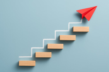 Poster - Progress and growth are depicted by a red paper airplane ascending a staircase formed by wooden blocks connected by a chalk-drawn path symbolizing business advancement and strategic development