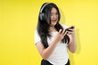 © Freddy Chandra - young asian woman playing mobile games with her headphone in yellow studio background