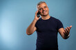 © Nenad - Oh, great news! Smiling mature casual man talking on the phone on the blue background. Isolated.