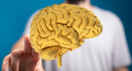 Poster - Stock photo of a golden brain model held in a hand, symbolizing intelligence, ideas, and innovation.