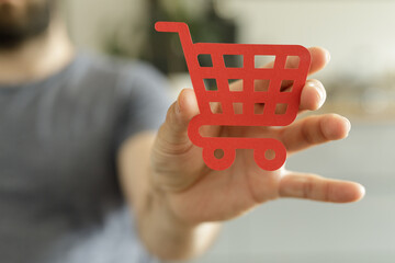 Aufkleber - Close-up of a hand holding a red paper shopping cart icon.  E-commerce, online shopping concept.
