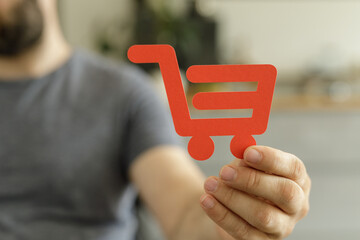 Aufkleber - Close-up of a man's hand holding a red paper shopping cart icon.  E-commerce, online shopping concept.
