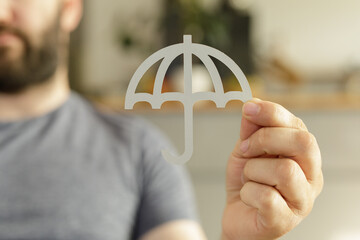 Poster - Image depicts a man holding a paper umbrella, symbolizing protection, insurance, or safety.