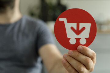 Aufkleber - Person holding a red circle with a shopping cart and download arrow icon.  Perfect for e-commerce, online shopping, and digital marketing.