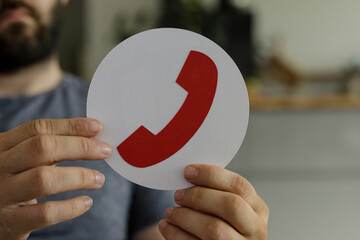 Poster - Close-up of a man's hands holding a paper circle with a red phone icon.  Contact us concept.