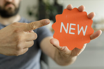 Poster - Close-up of a man's hand pointing at an orange 'NEW' sign.  Perfect for new product launches or announcements.