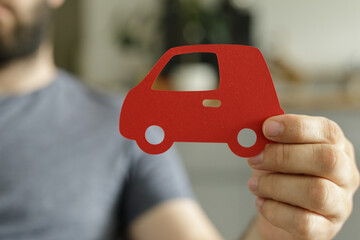 Poster - Close-up of a man holding a red paper car, symbolizing auto insurance, new car purchase, or car loan.