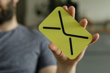Aufkleber - Close-up of a hand holding a yellow card with a simple envelope icon.  Concept for communication, email, message.
